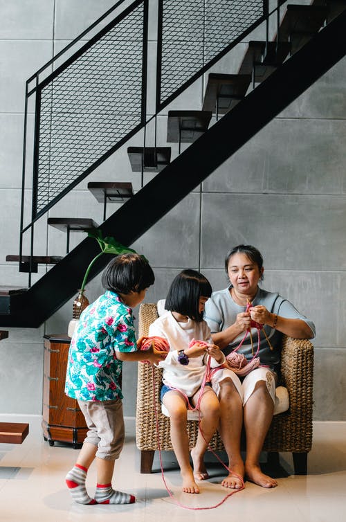 亚洲孩子帮助祖母和妹妹编织在扶手椅上 · 免费素材图片
