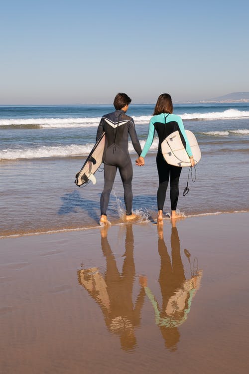 男人和女人抱着白色和黑色的冲浪板，在海滩上行走 · 免费素材图片