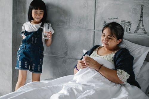 可爱的族裔孩子给杯水躺在床上的生病的祖母 · 免费素材图片