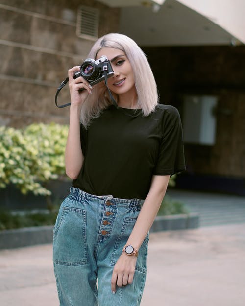 黑色的t恤和蓝色的牛仔牛仔裤，拿着黑色的单反相机的女人 · 免费素材图片