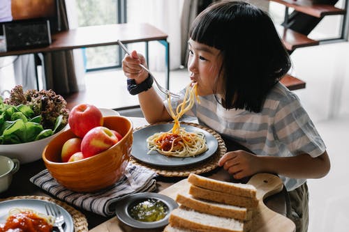 可爱的亚洲小女孩在午餐期间在家享受美味的意大利面 · 免费素材图片