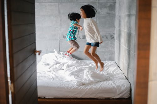 有趣的赤脚小族裔兄弟姐妹在床上跳 · 免费素材图片