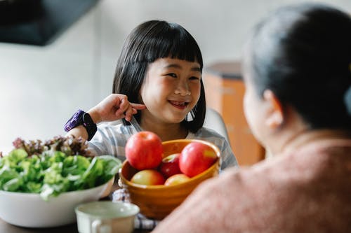 微笑的滑稽的亚裔女孩微笑着，当与母亲一起吃早餐时 · 免费素材图片