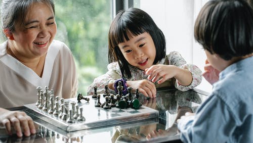 可爱的亚洲孩子在积极的祖母的帮助下下棋 · 免费素材图片