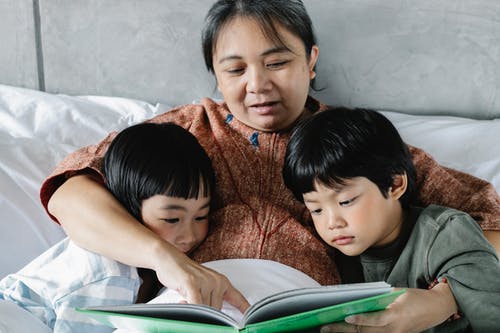 族裔母亲和小孩在床上看书 · 免费素材图片