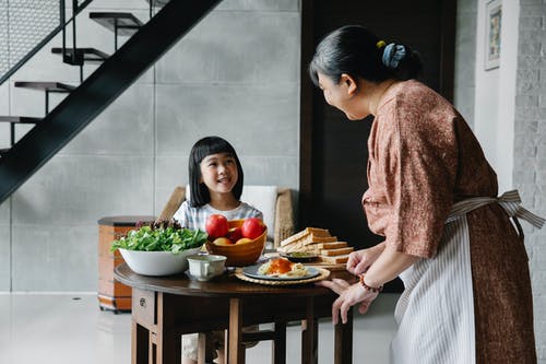 高兴的小亚洲女孩在家吃午饭时微笑着和祖母说话 · 免费素材图片