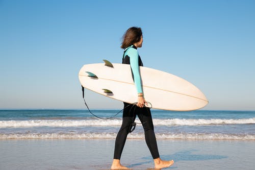 拿着白色冲浪板的蓝色长袖衬衣的妇女站立在海滩 · 免费素材图片