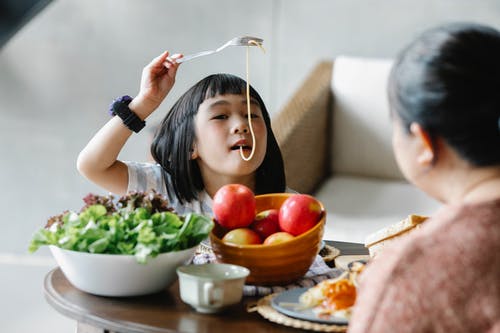 有趣的族裔孩子和祖母共进午餐期间吃意大利面 · 免费素材图片