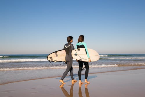 男人和女人抱着白色的冲浪板，在海滩上行走 · 免费素材图片