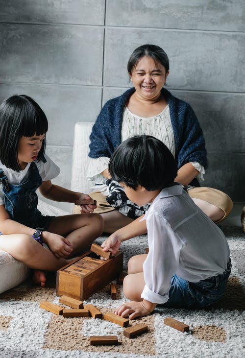集中玩塔游戏的亚洲孩子坐在开朗的祖母附近的地板上 · 免费素材图片