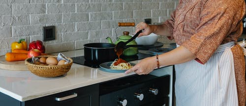 裁剪无法识别的家庭主妇在厨房里的意大利面条中添加番茄酱 · 免费素材图片