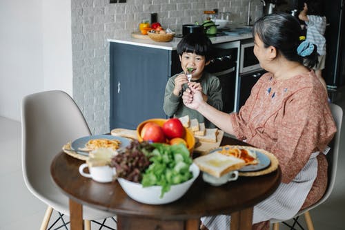 性格开朗的小亚洲男孩在家里吃早餐和亲切的祖母 · 免费素材图片
