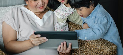 匿名的亚裔女子和孙子们在平板电脑上观看视频 · 免费素材图片