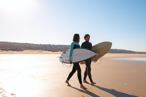 男子携带白色冲浪板在海滩上行走 · 免费素材图片