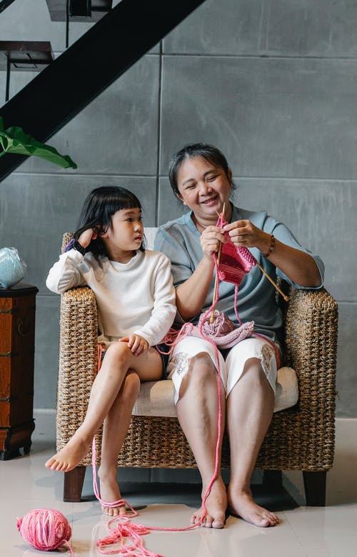 正面资深亚洲女性编织，当坐与逗人喜爱的孙女的扶手椅子时 · 免费素材图片
