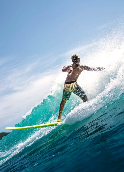不可识别的赤膊运动型家伙骑波在冲浪板上在阳光下 · 免费素材图片