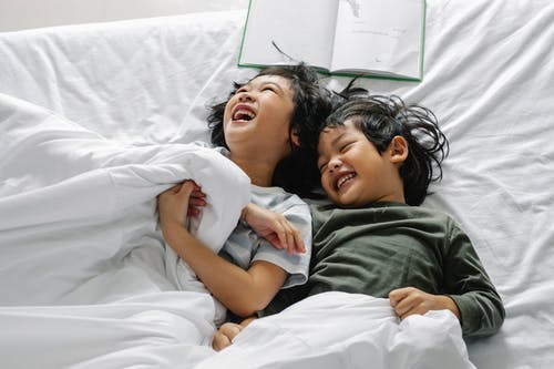 族裔孩子躺在床上笑 · 免费素材图片