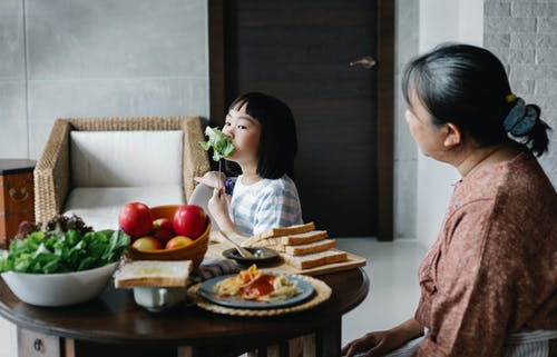 亚洲小姑娘坐在餐桌旁和祖母一起吃健康的沙拉 · 免费素材图片