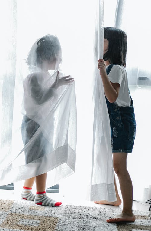 匿名儿童躲在家里的窗帘后面 · 免费素材图片