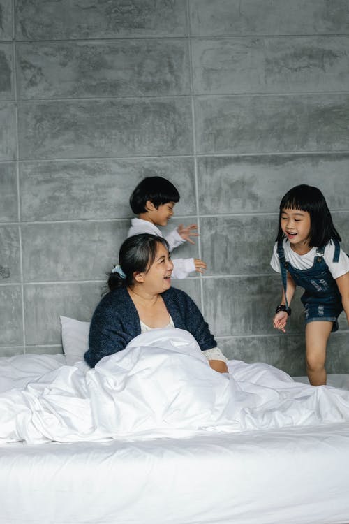 活跃的孩子在祖母周围的床上奔跑 · 免费素材图片