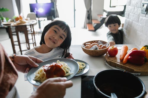 在厨房里等待午餐的开朗可爱的亚洲孩子 · 免费素材图片