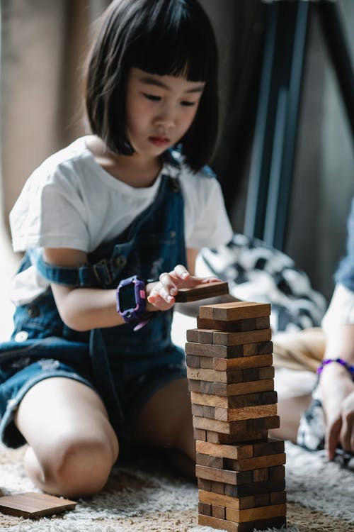 严重的亚洲孩子玩塔游戏坐在地毯上 · 免费素材图片