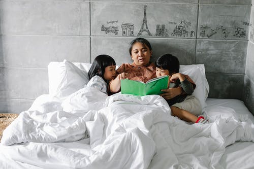 可爱的种族孩子拥抱祖母和听故事，而躺在床上在时尚的公寓 · 免费素材图片