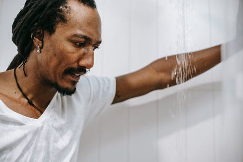 沮丧的年轻族裔男性，倚在淋浴间的墙上 · 免费素材图片