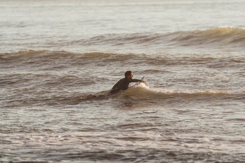 男子与冲浪板在波浪海洋中游泳 · 免费素材图片