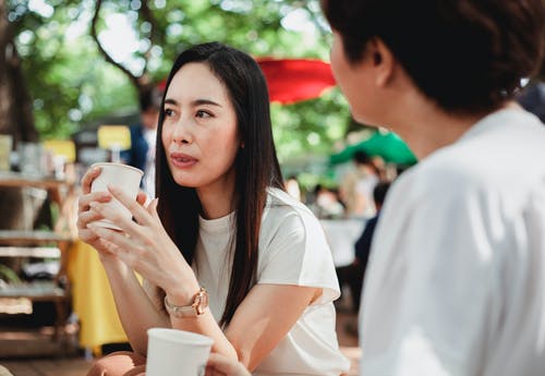 积极的亚裔妇女在阳光明媚的街头市场喝咖啡休息时间 · 免费素材图片