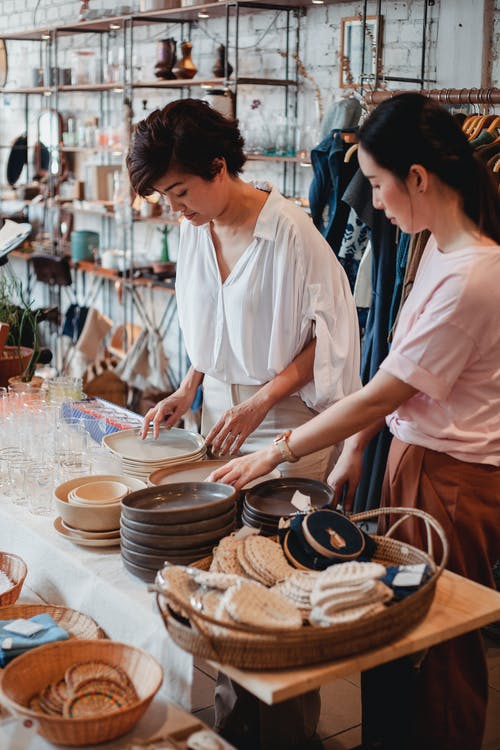 族裔女友在店里选择桌上的盘子 · 免费素材图片