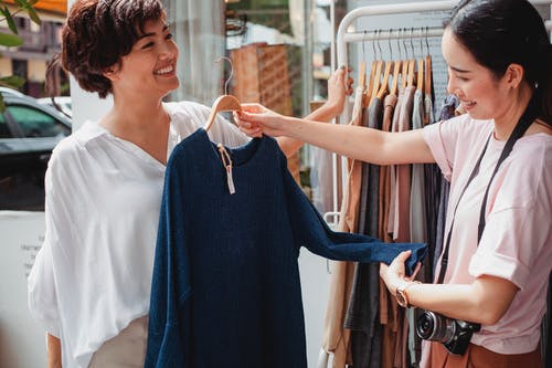 与女友在街边小店里挑选衣服的作物亚洲买家 · 免费素材图片