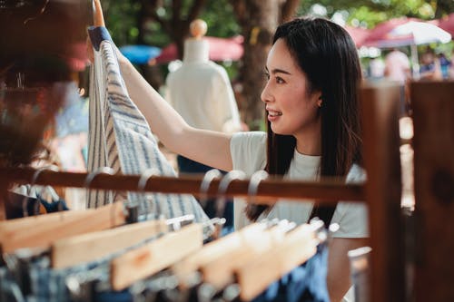 年轻的亚裔女子在街头市场上选择衣服 · 免费素材图片