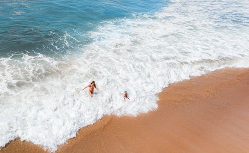 匿名的女人，在有沙质海岸的强大海洋中享受阳光灿烂的夏天的一天 · 免费素材图片