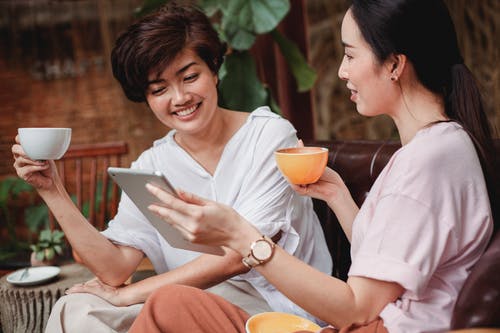 积极的亚洲朋友浏览平板电脑，喝咖啡 · 免费素材图片