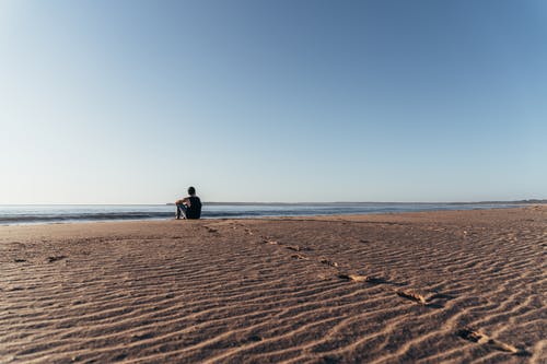 不可识别的人坐在沙滩上，享受海景 · 免费素材图片