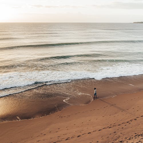 日落时分在沙滩上放松的匿名旅行者 · 免费素材图片