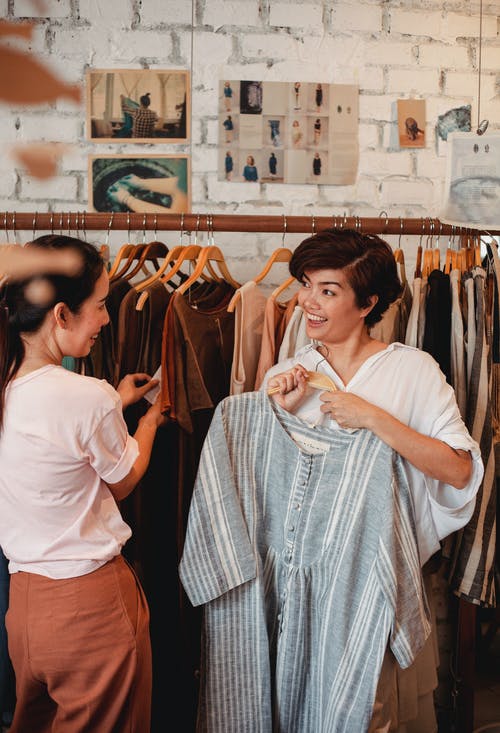 开朗的亚洲女性购物者在商店里选择衣服时进行交互 · 免费素材图片