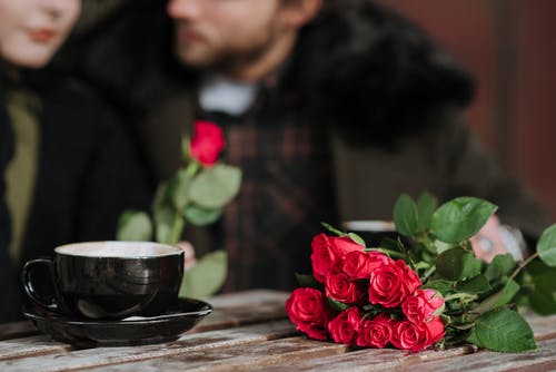 黑色陶瓷碗旁边棕色木桌上的红玫瑰 · 免费素材图片