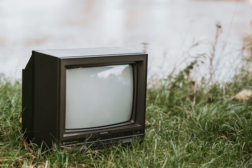 黑色crt电视在绿色草地上 · 免费素材图片