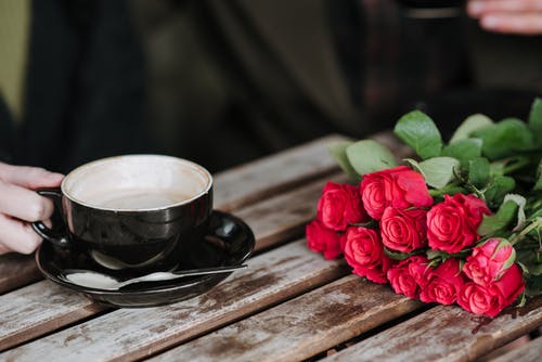 黑色玫瑰花花瓣旁边的飞碟上的黑色陶瓷茶杯 · 免费素材图片