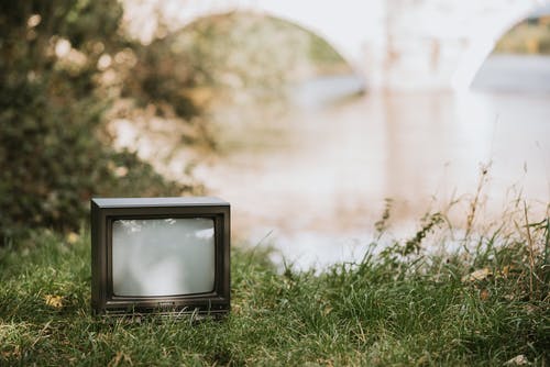 黑色crt电视在绿色草地上 · 免费素材图片