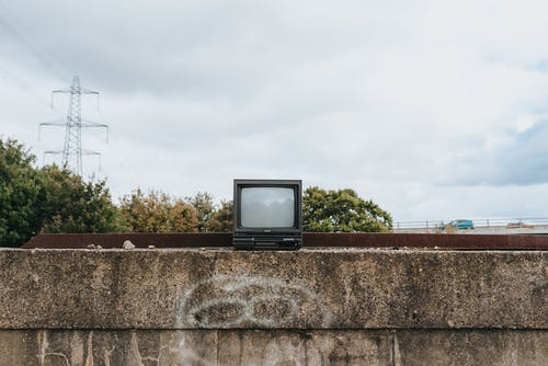 棕色混凝土墙上的黑色crt电视 · 免费素材图片