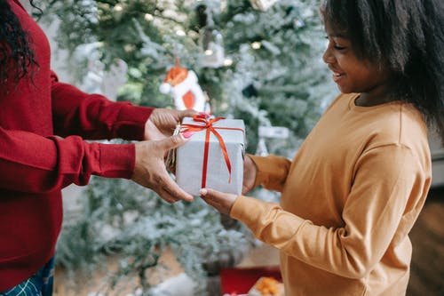 裁剪黑人母亲通过圣诞节礼物给微笑的女儿 · 免费素材图片