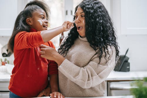 无忧无虑的黑人女孩在作物母亲脸上涂面粉 · 免费素材图片