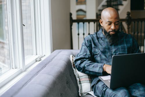 严重的黑人男子，在家中使用笔记本电脑 · 免费素材图片