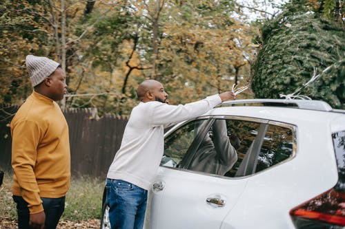 族裔人在儿子附近的车顶上绑枞树 · 免费素材图片