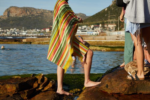 绿色红色和白色礼服站在水附近的棕色岩石上的女人 · 免费素材图片