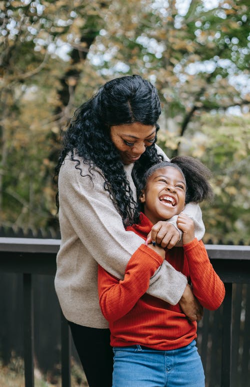 黑人母亲在栅栏附近拥抱快乐的女儿 · 免费素材图片