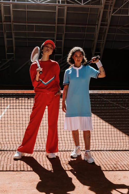 蓝色polo衫的男人站在红色长袖礼服的女人旁边拿着网球拍 · 免费素材图片